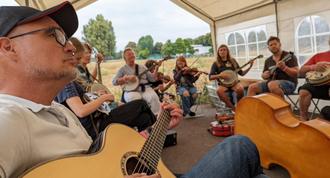 Bluegrass-Workshop auf dem Festival, eine Gruppe Musiker*innen sitzt im Zelt, ein Bass liegt in der Mitte